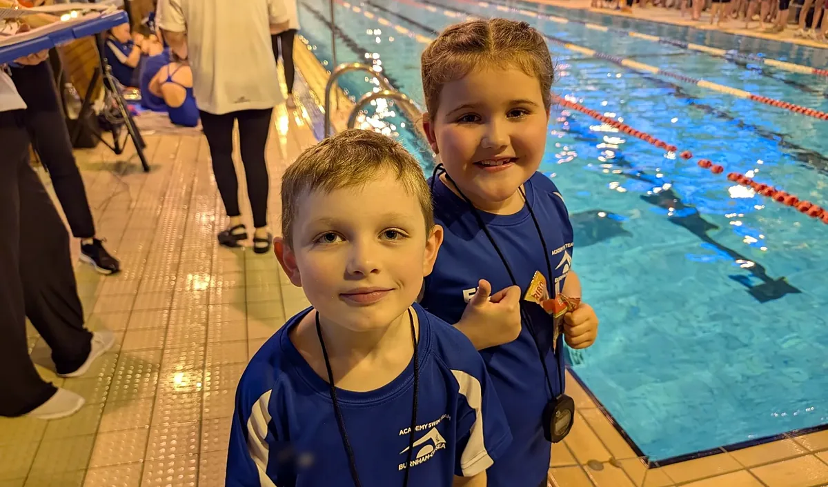 Two young swimmers in club kit smiling at the side of the pool