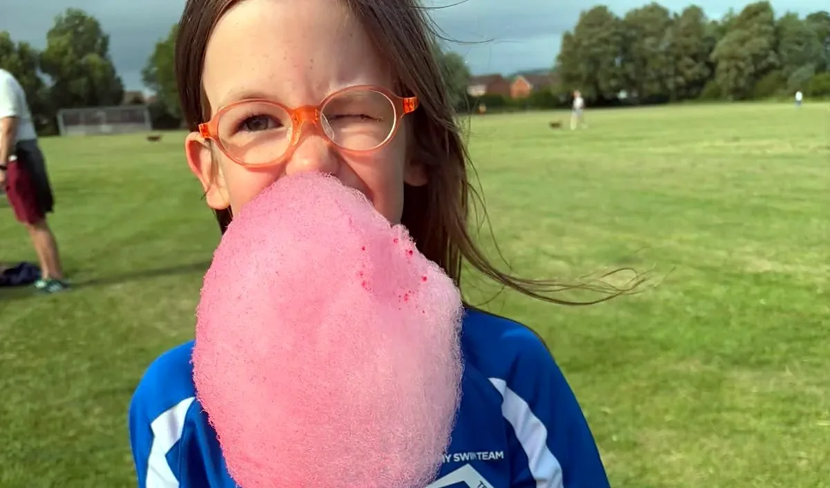 A young swimmer in club kit winking behind a big pink stick of candy floss at a club event