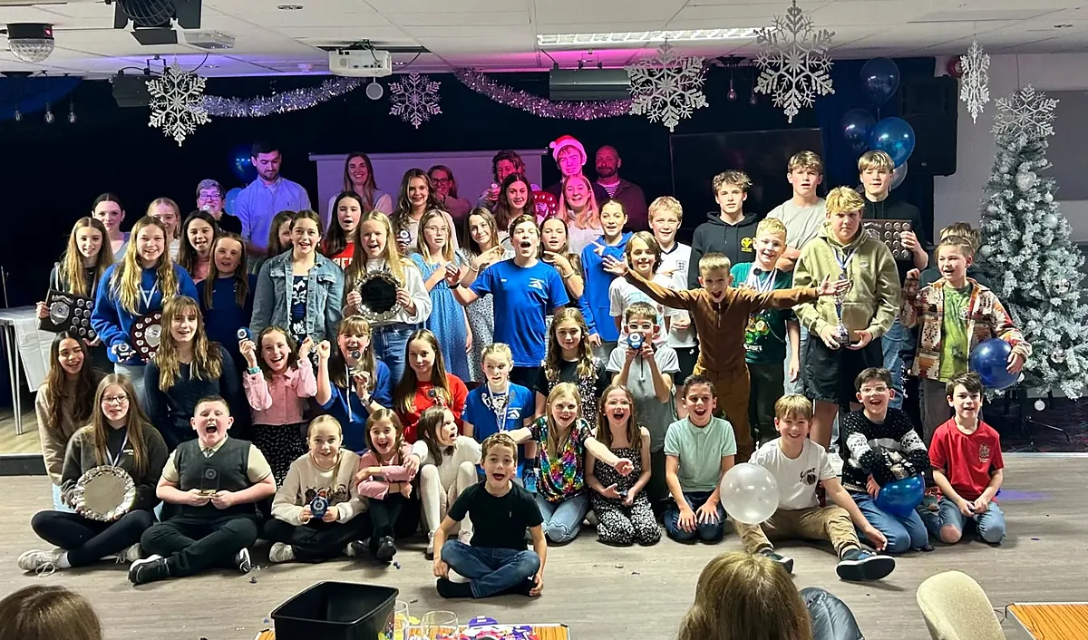 A large group of swimmers and families celebrating together at the club presentation evening, holding trophies and medals