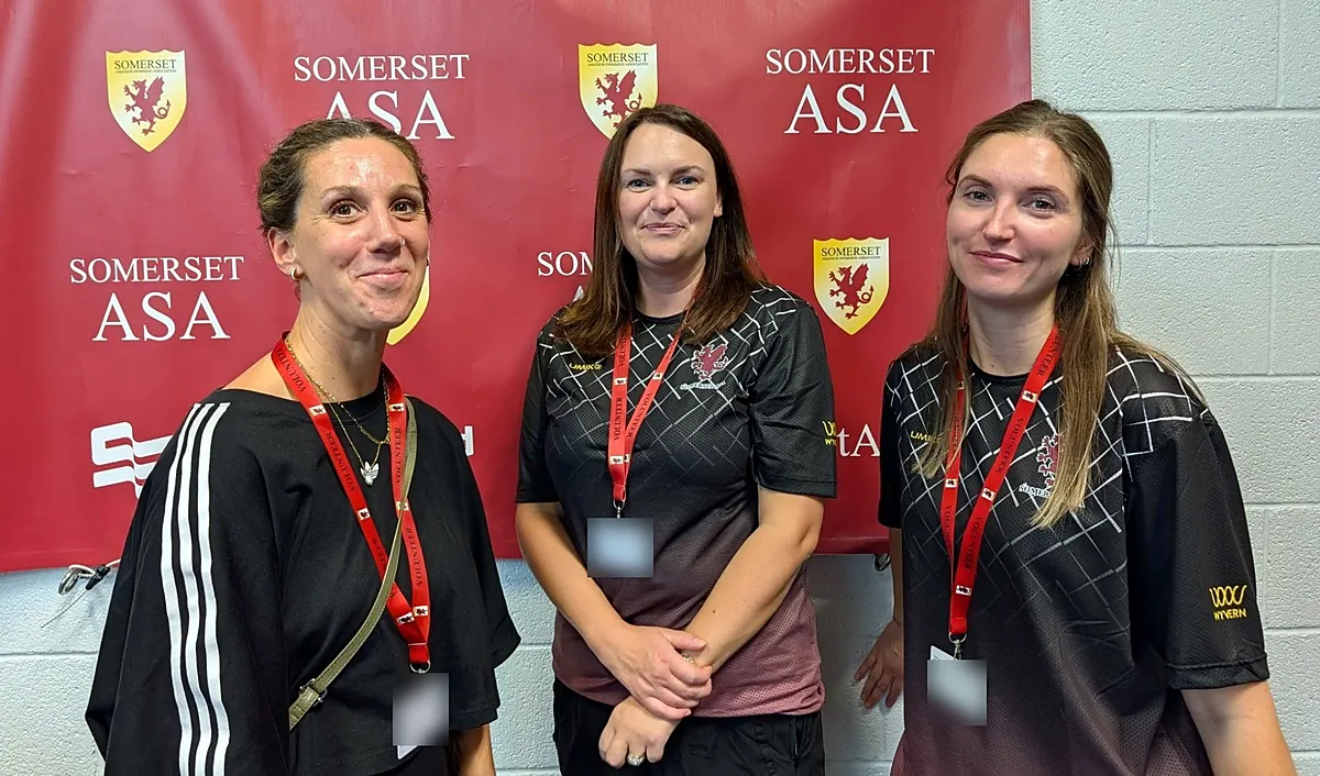 Three volunteers wearing red volunteer lanyards in front of a Somerset ASA banner